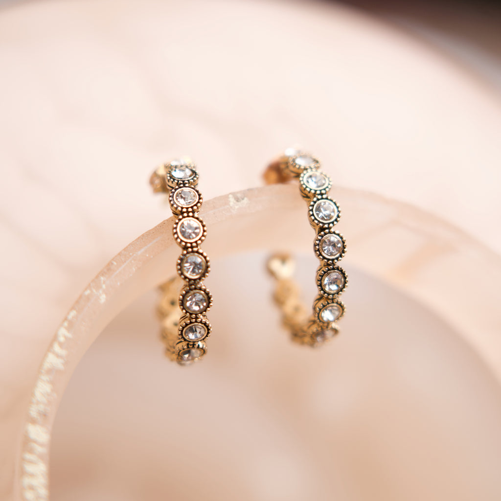 Pair of gold hoop earrings with embedded stones on a soft pink background