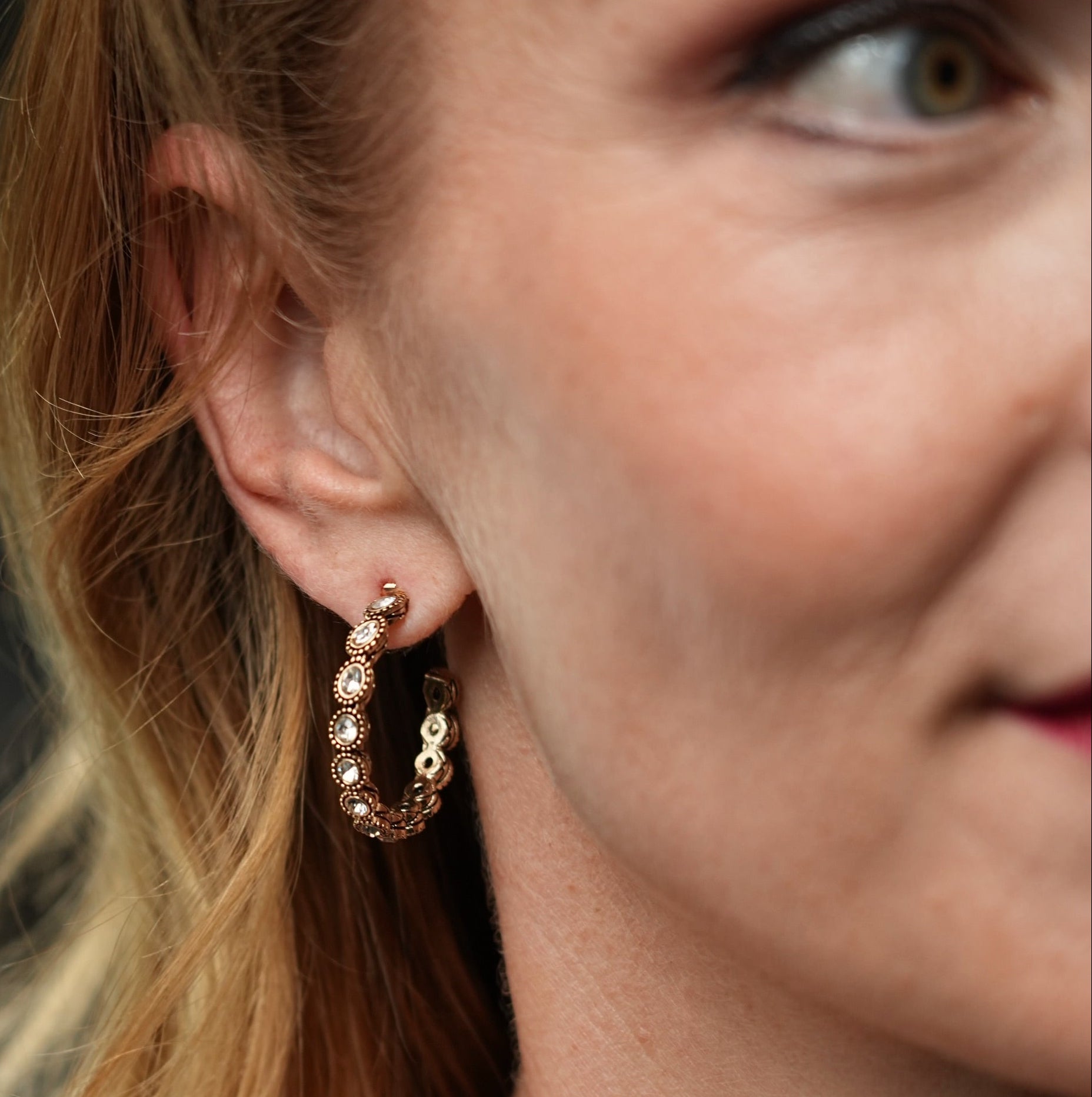 Close-up of a woman wearing gold hoop earrings with a blurred background