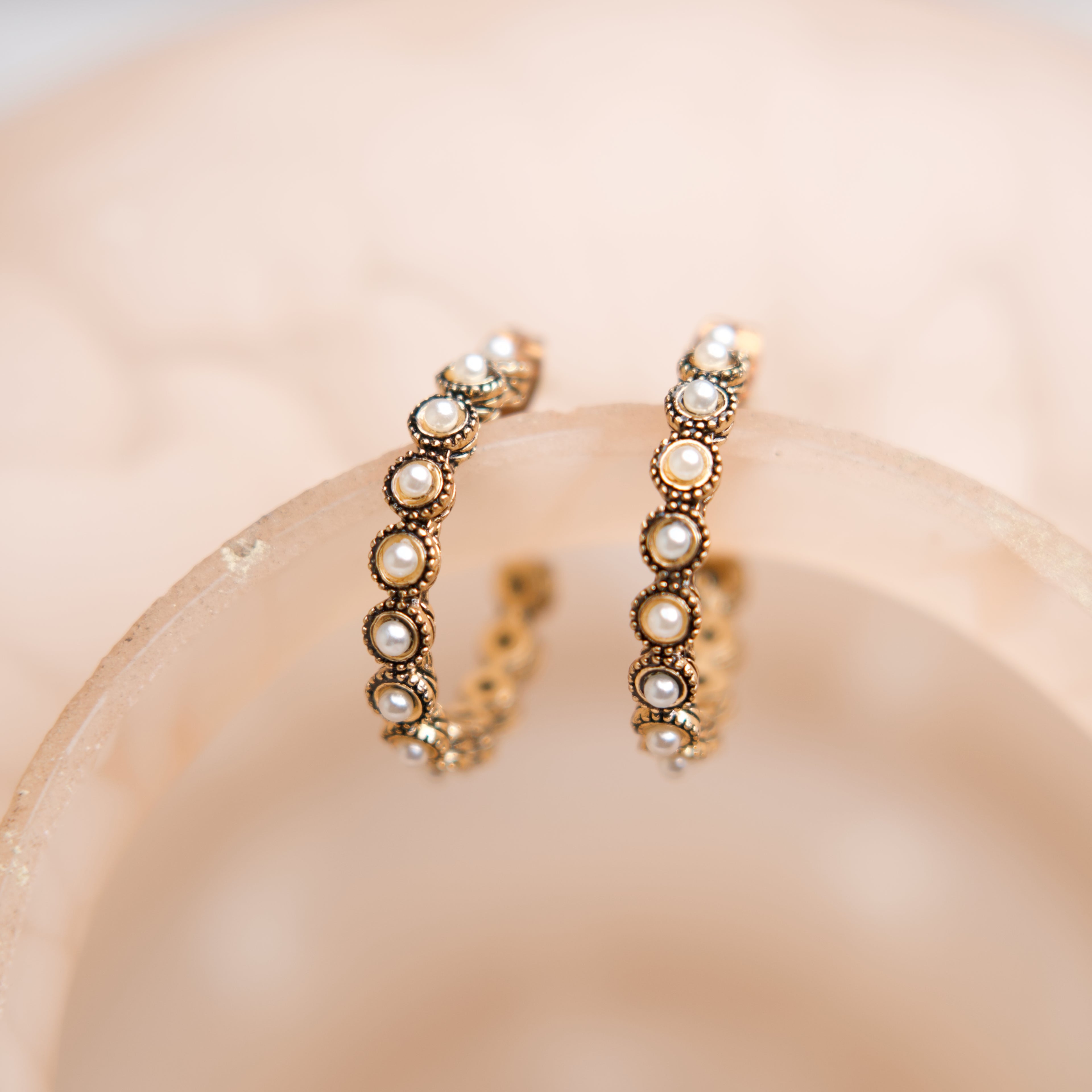 Pair of pearl hoop earrings on a soft pink background
