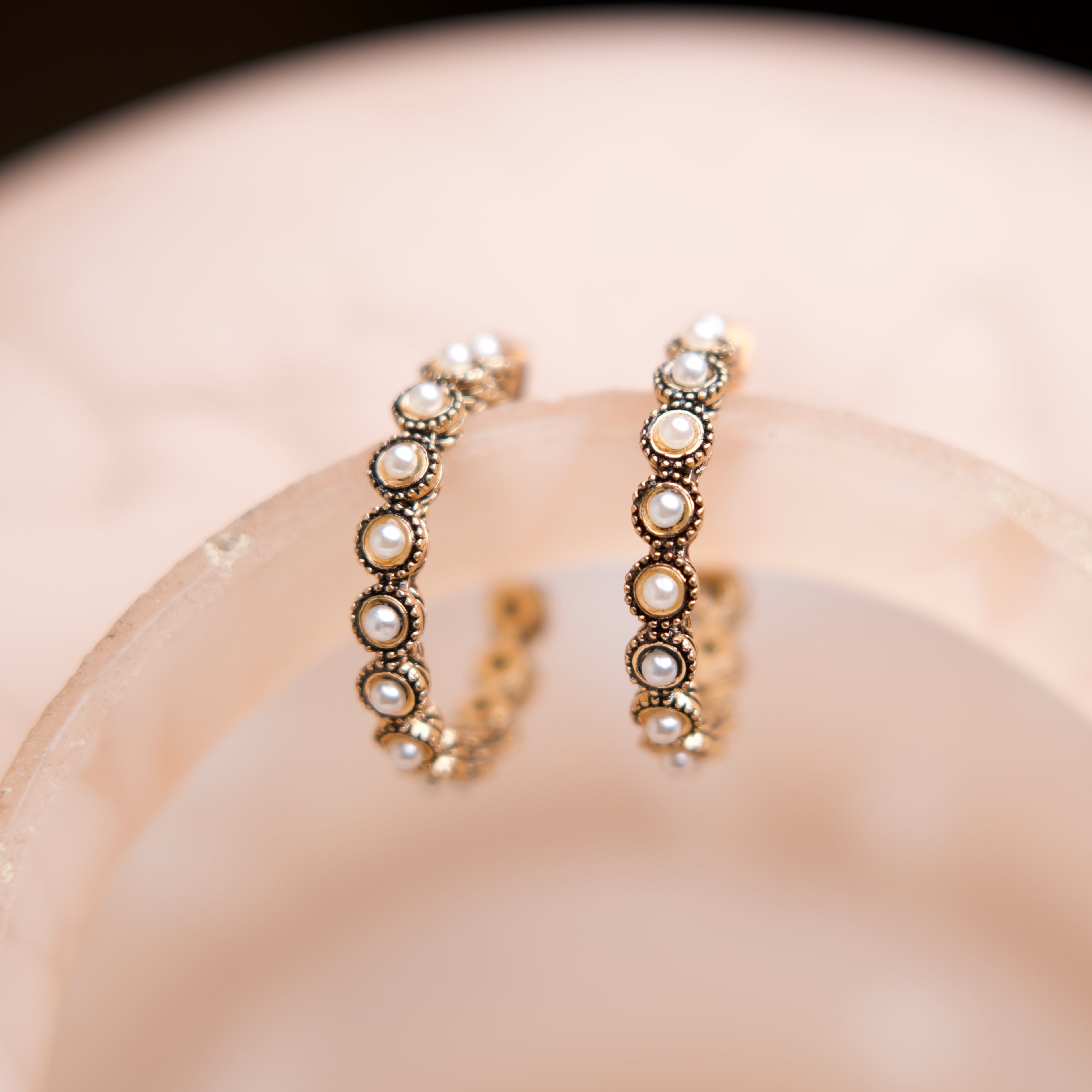 Pair of gold hoop earrings with pearls on a soft pink background