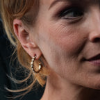 Close-up of a woman wearing gold hoop earrings with a dark background