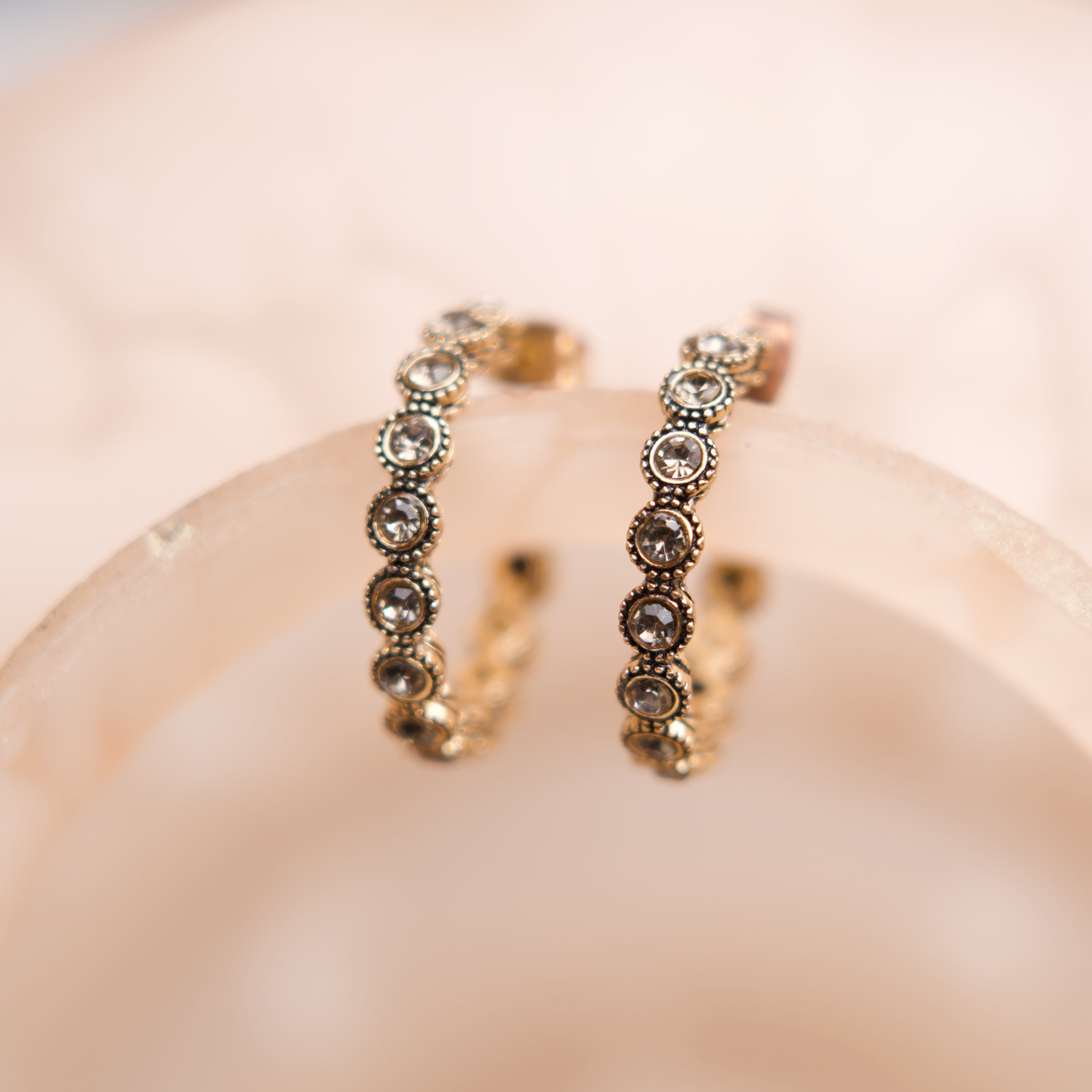 Pair of gold hoop earrings with embedded stones on a soft pink background
