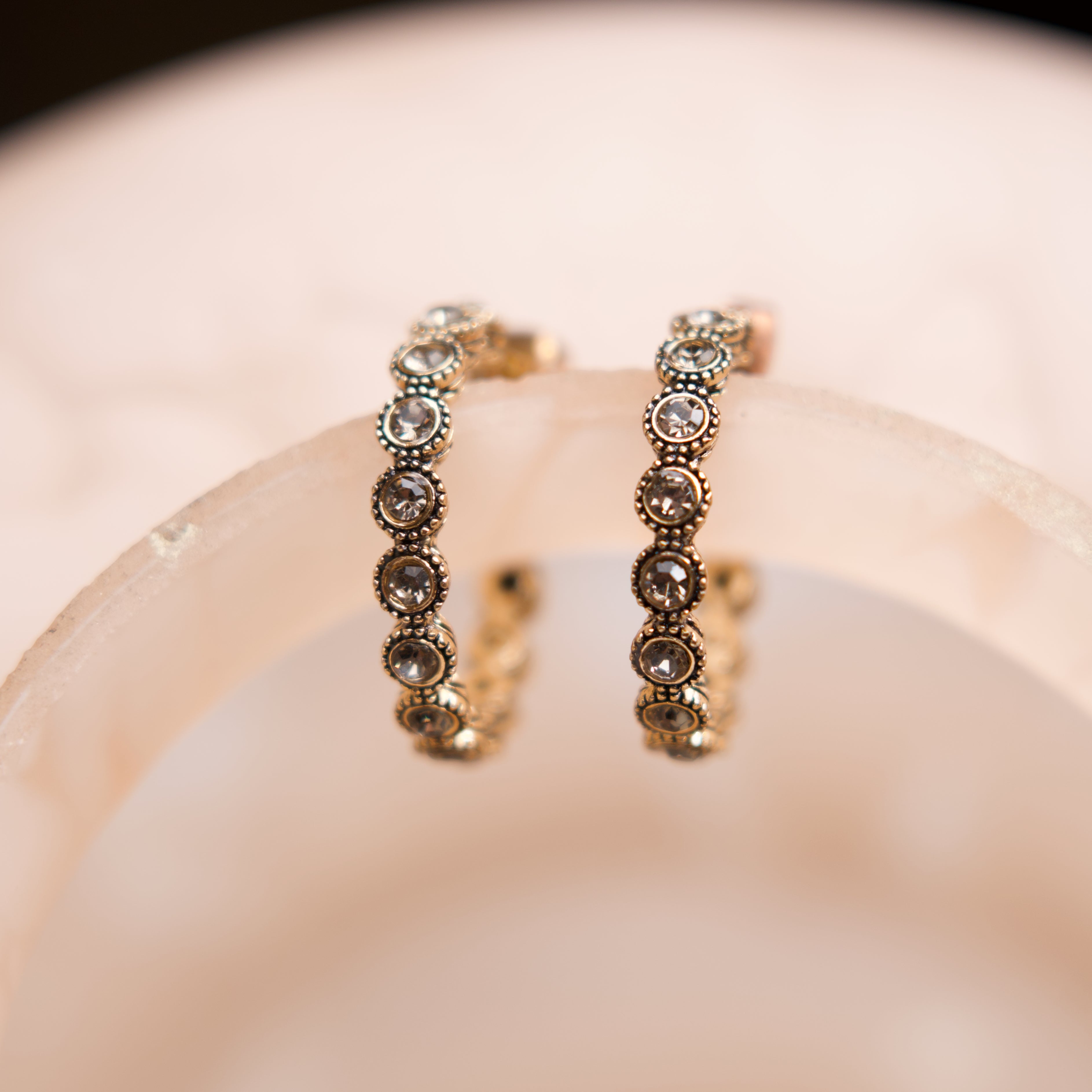 Pair of gold hoop earrings with embedded stones on a soft pink background