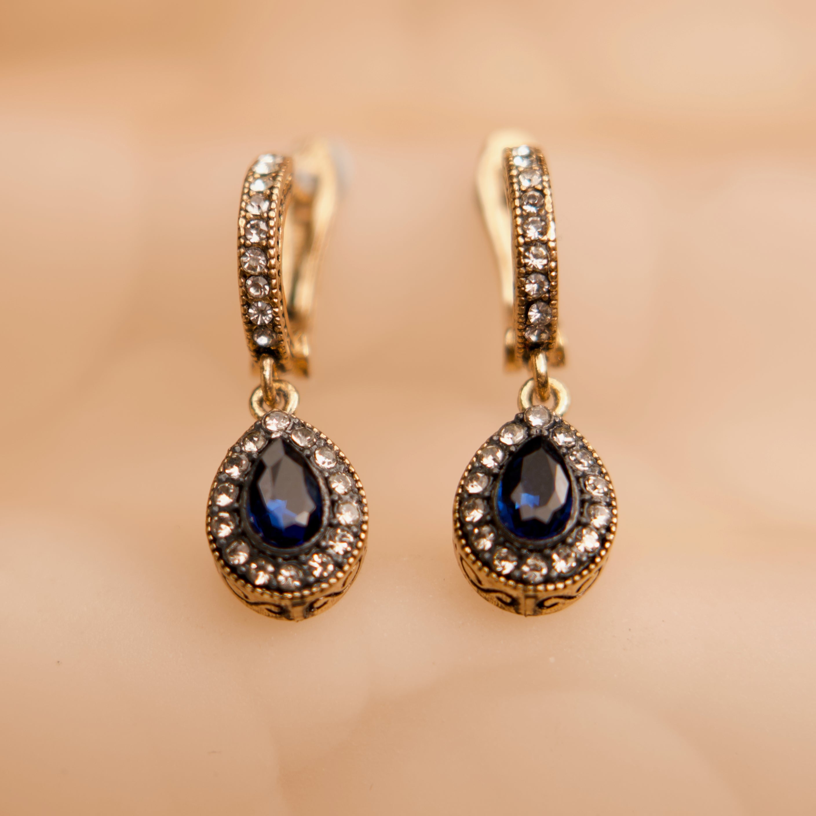Gold earrings with blue gemstones on a beige background