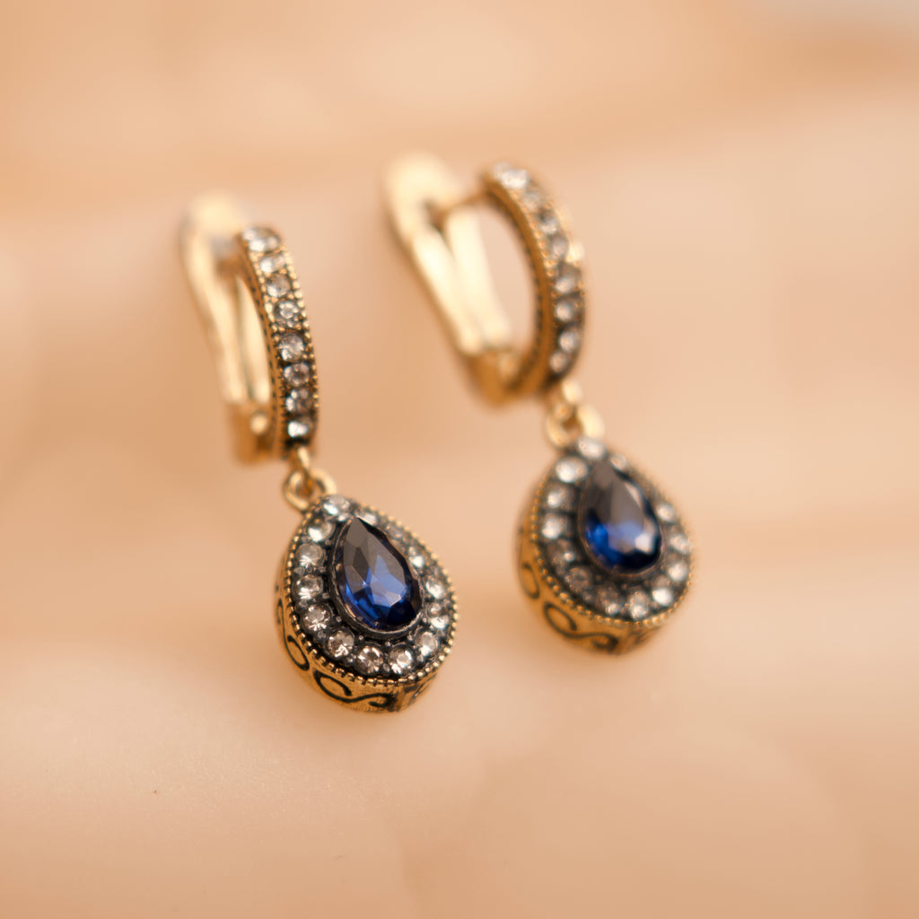 Gold earrings with blue gemstones on a blurred background