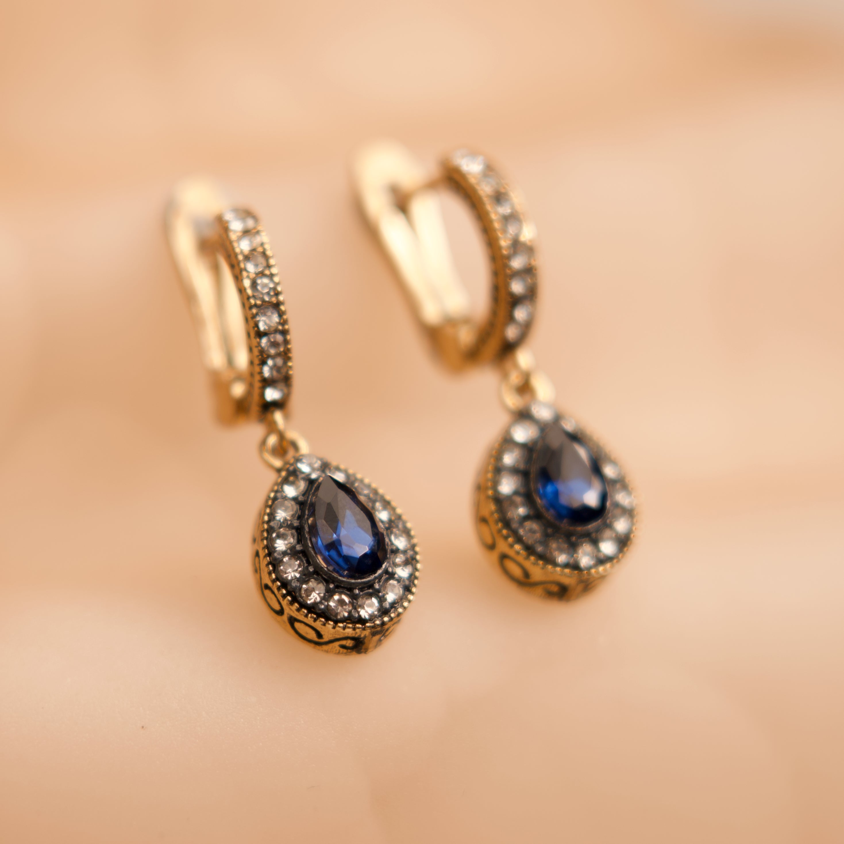 Gold earrings with blue gemstones on a blurred background