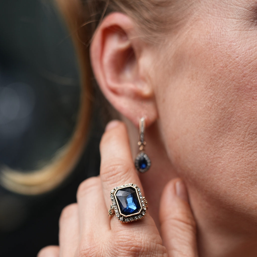 Close-up of a person wearing a blue gemstone ring and earring.