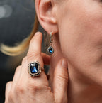Close-up of a woman wearing a blue gemstone ring and earring, with a blurred background.