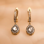 Gold earrings with clear gemstones on a beige background