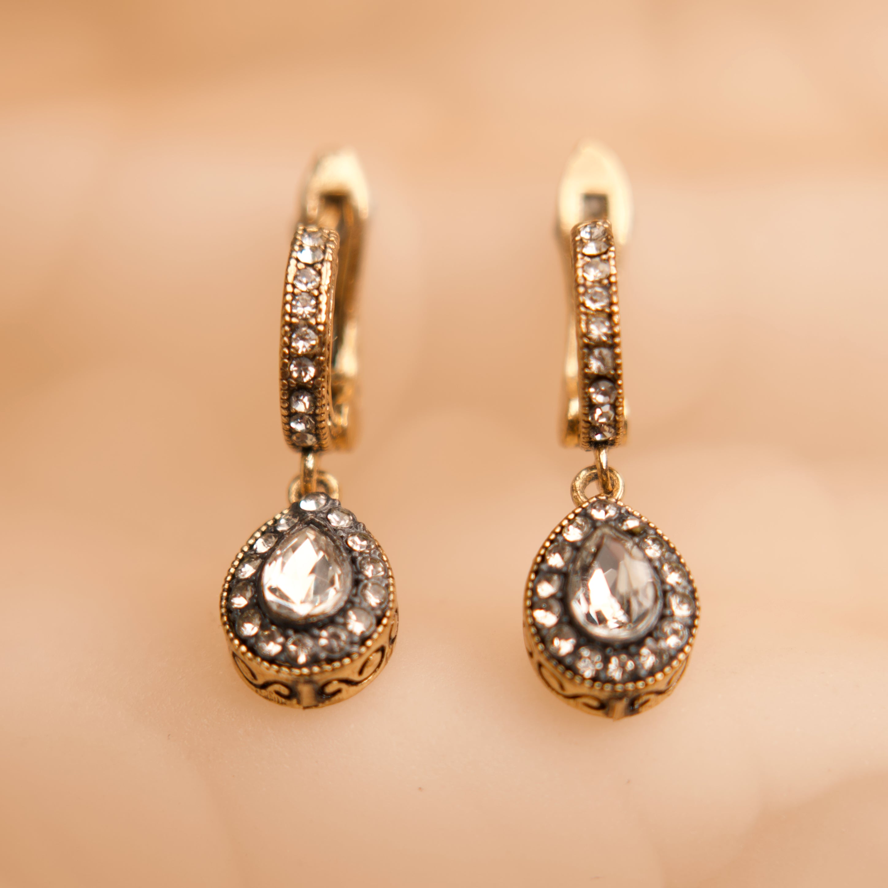 Gold earrings with clear gemstones on a beige background