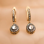 Pair of gold earrings with clear gemstones on a beige background