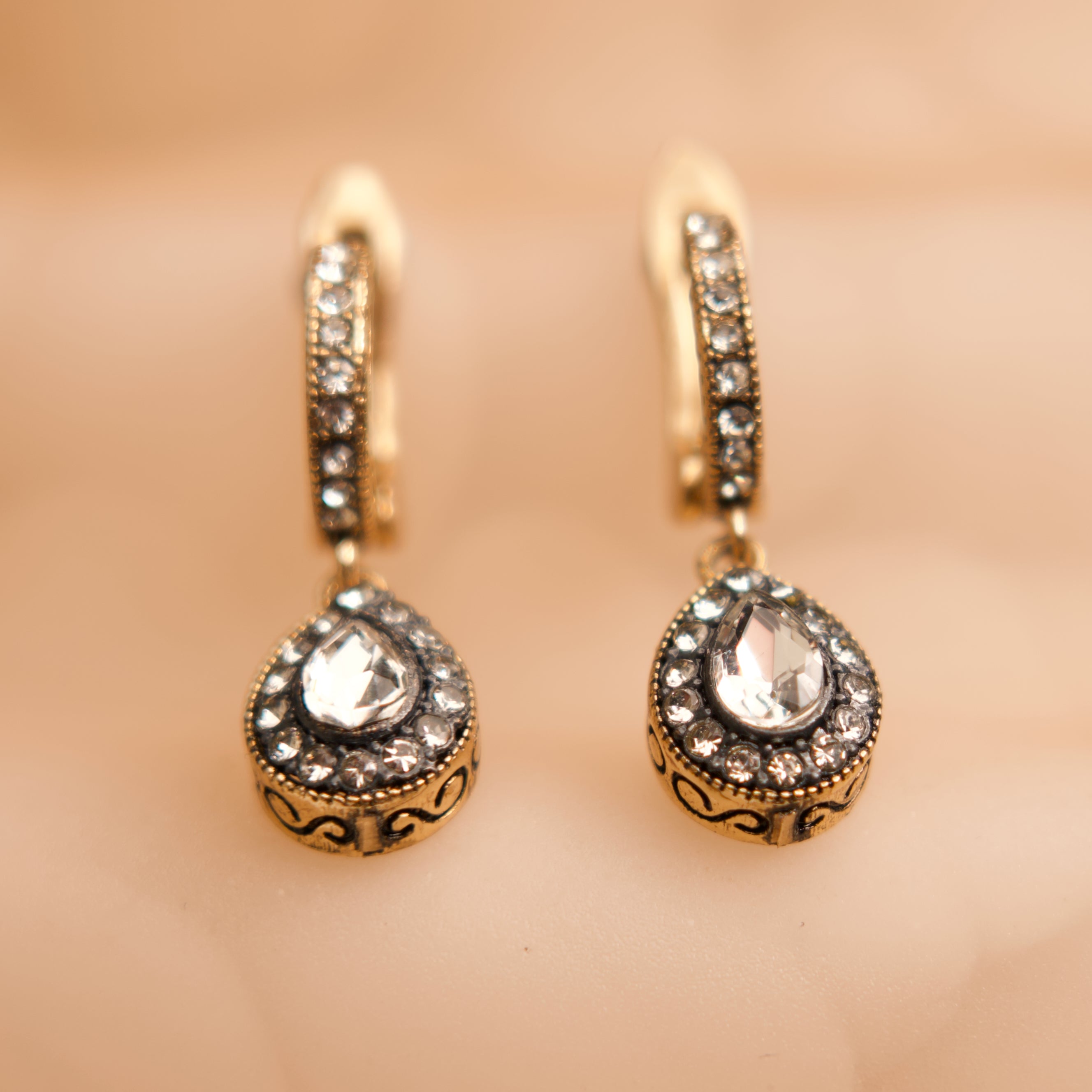 Pair of gold earrings with clear gemstones on a beige background