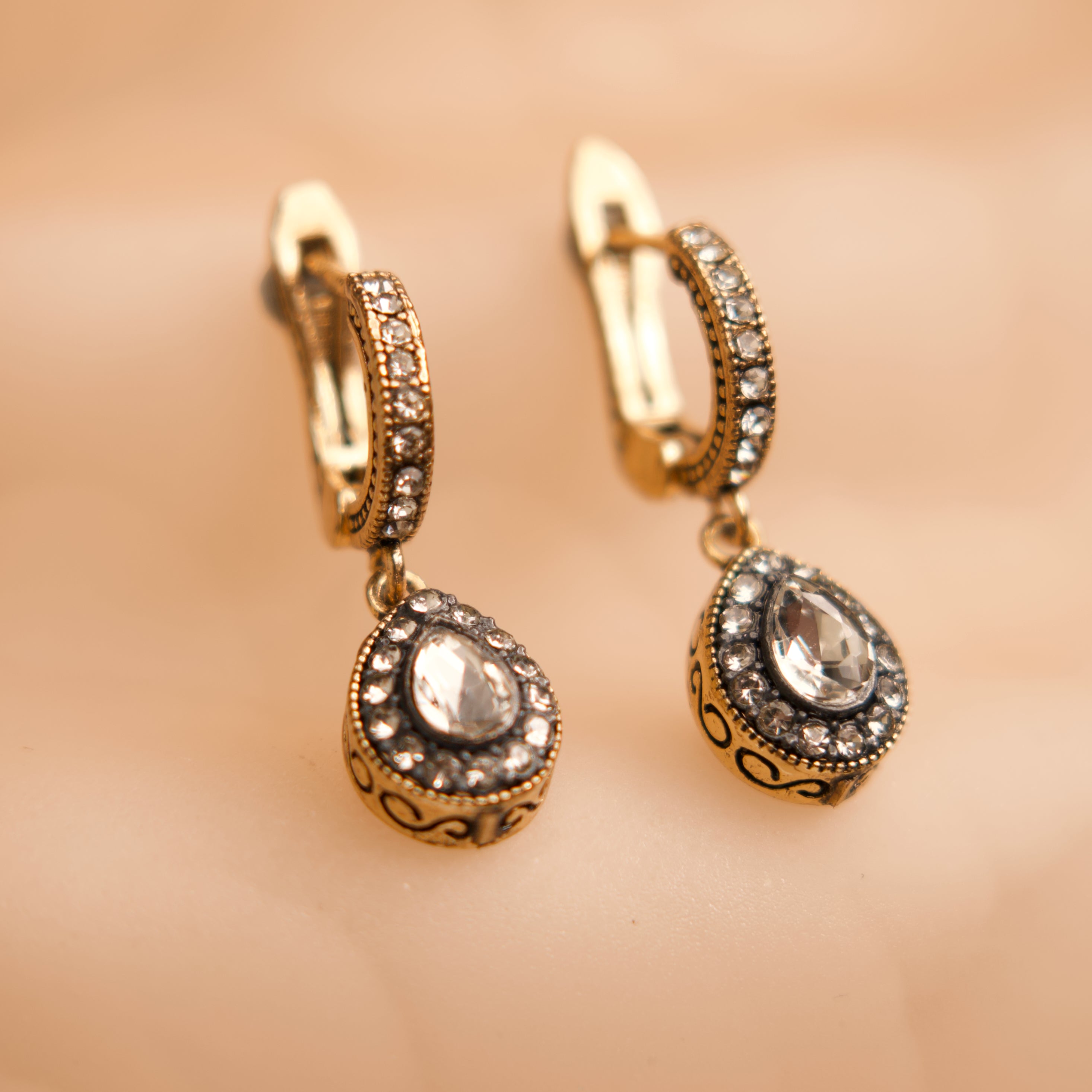 Gold hoop earrings with teardrop-shaped gemstones on a beige background