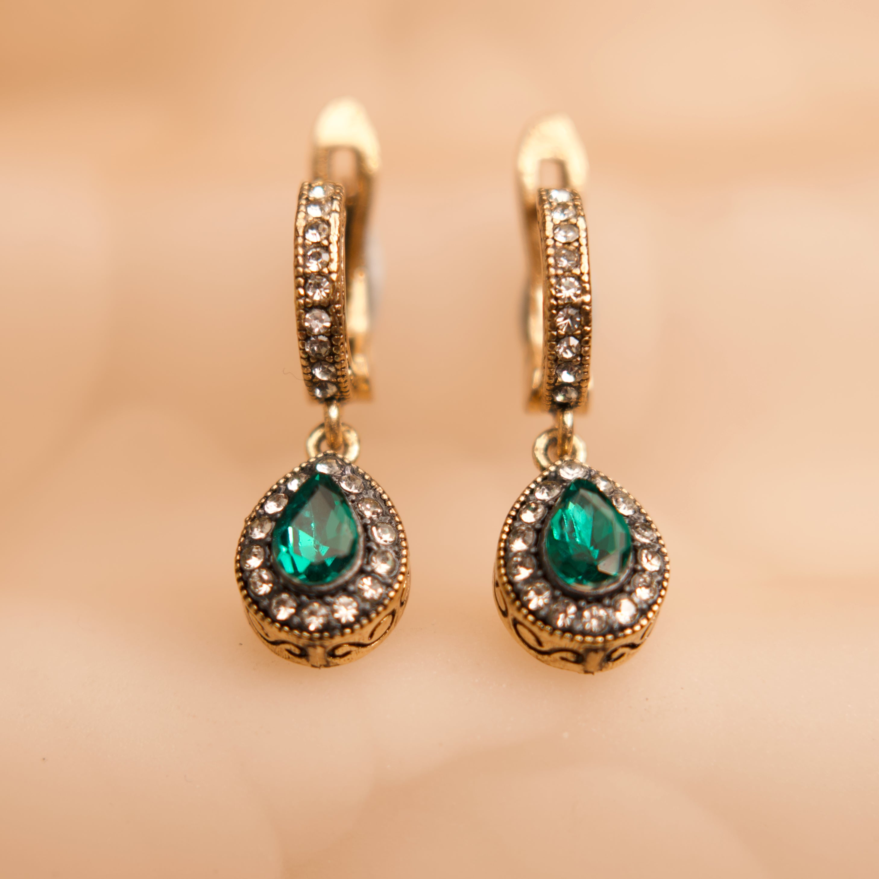 Gold hoop earrings with green gemstones on a beige background