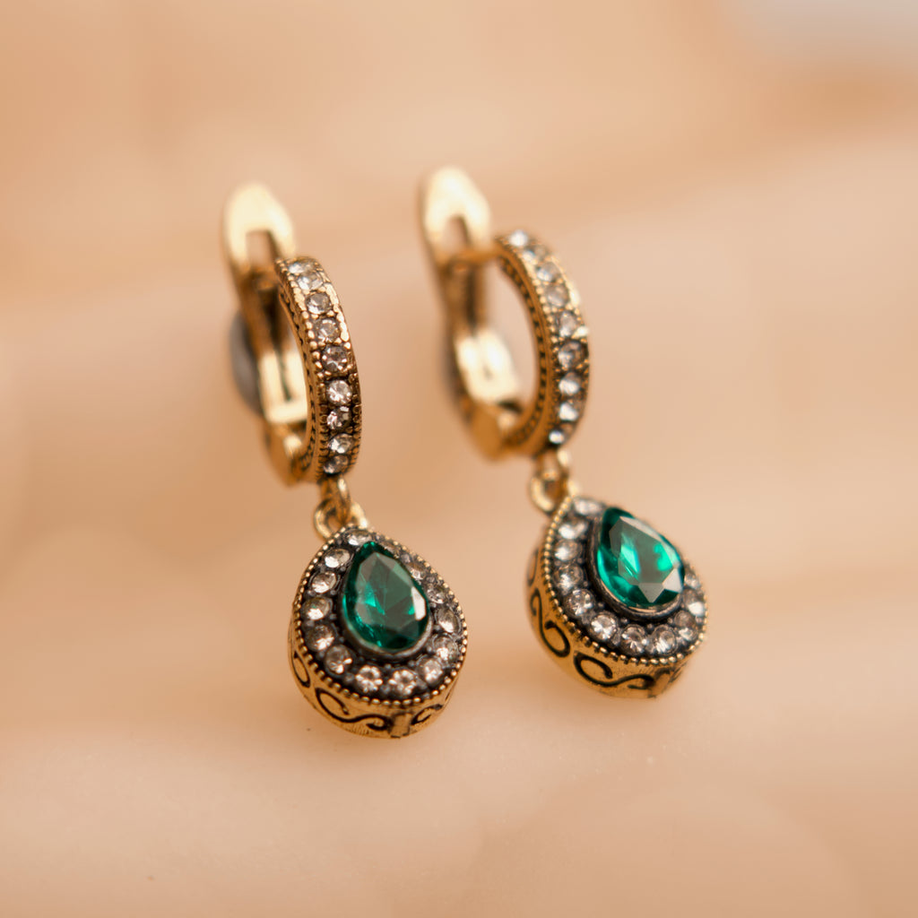 Gold hoop earrings with green gemstones on a beige background