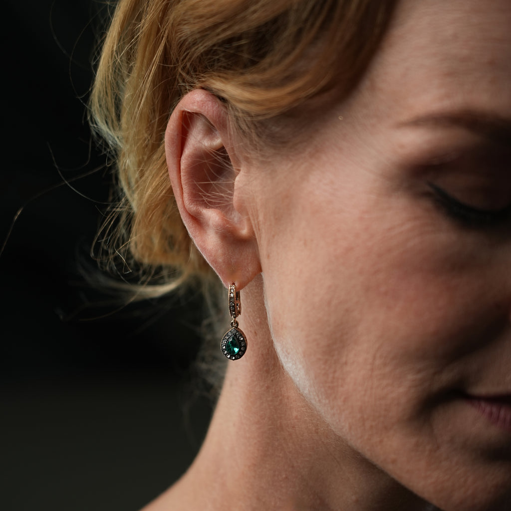 Close-up of a woman wearing a green gemstone earring against a dark background