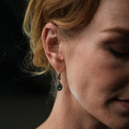 Close-up of a woman wearing a green gemstone earring against a dark background