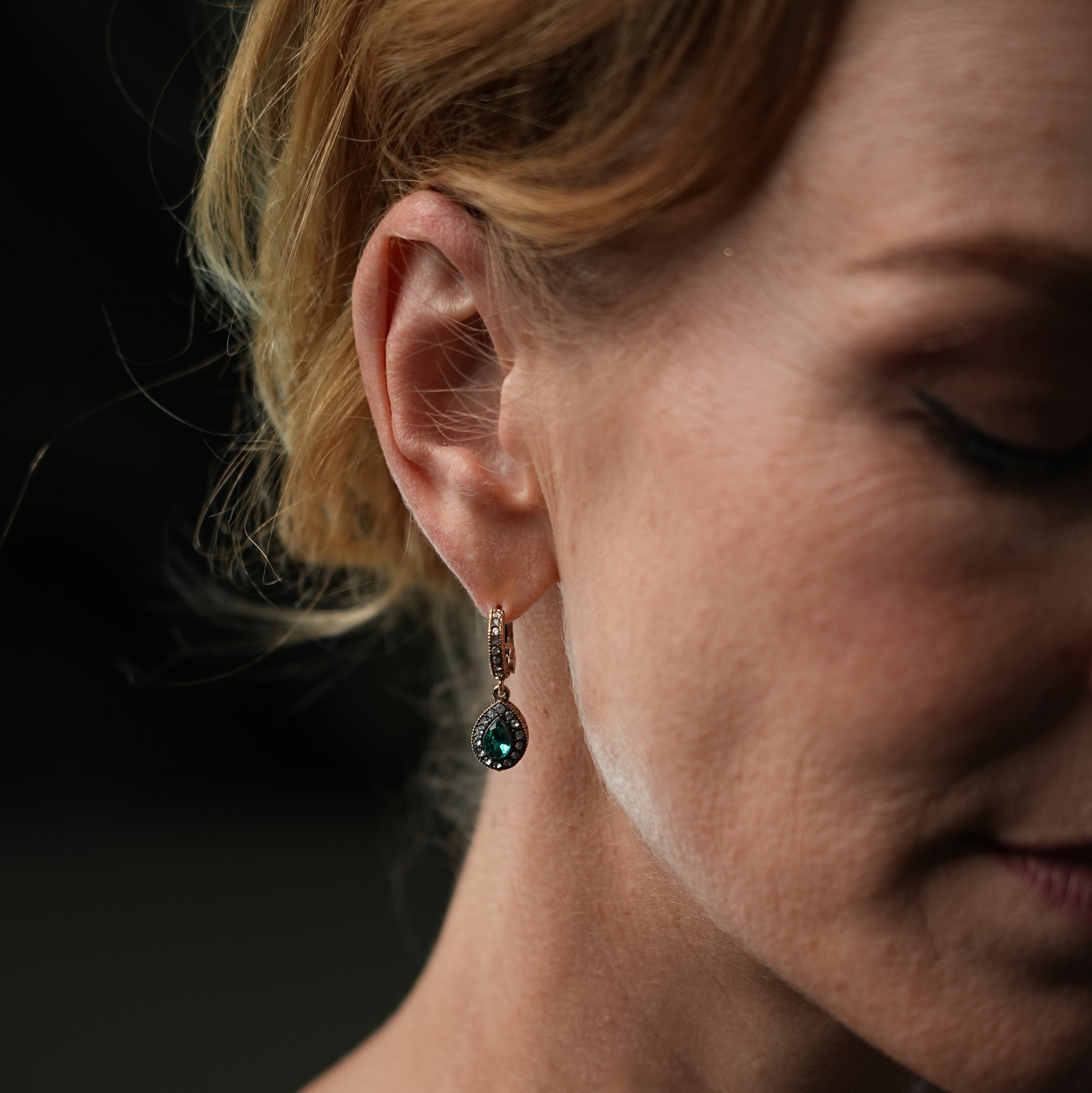 Close-up of a woman wearing a green gemstone earring against a dark background