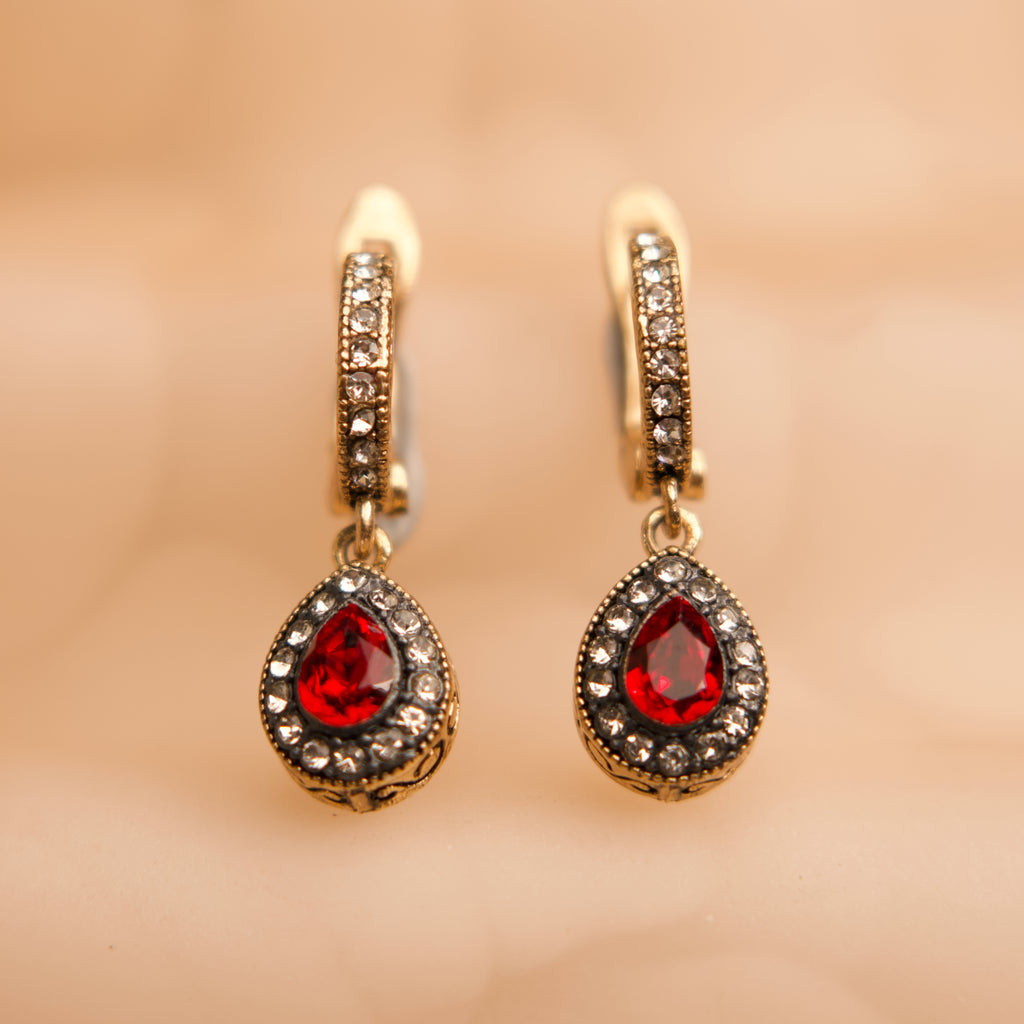 Gold earrings with red gemstones on a beige background