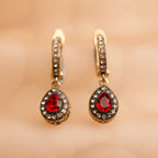 Gold earrings with red gemstones on a beige background