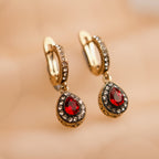 Gold hoop earrings with red gemstones on a beige background