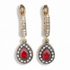 Pair of earrings with red teardrop stones and gold accents on a white background