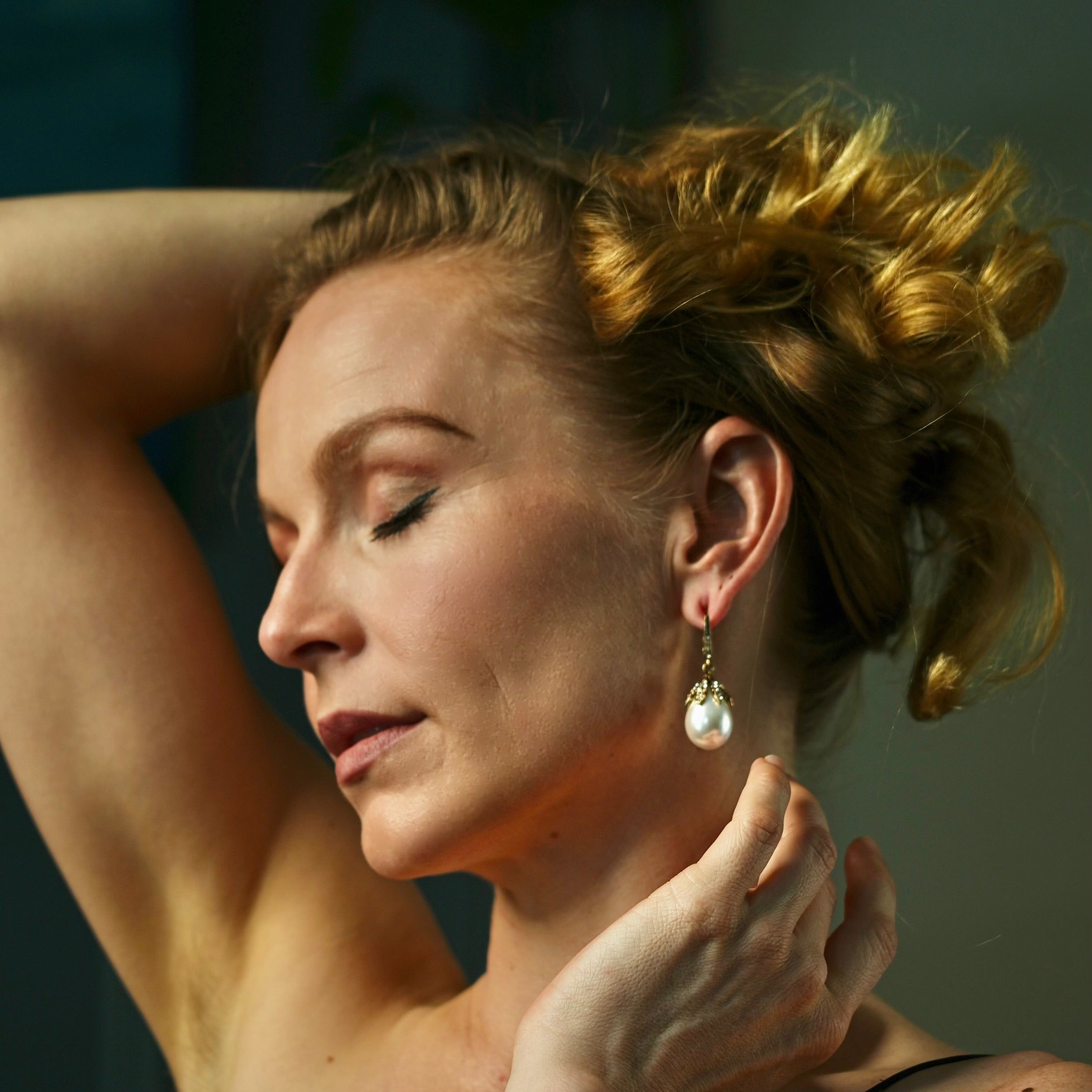 Woman with styled hair and earrings, wearing a bracelet, against a blurred background