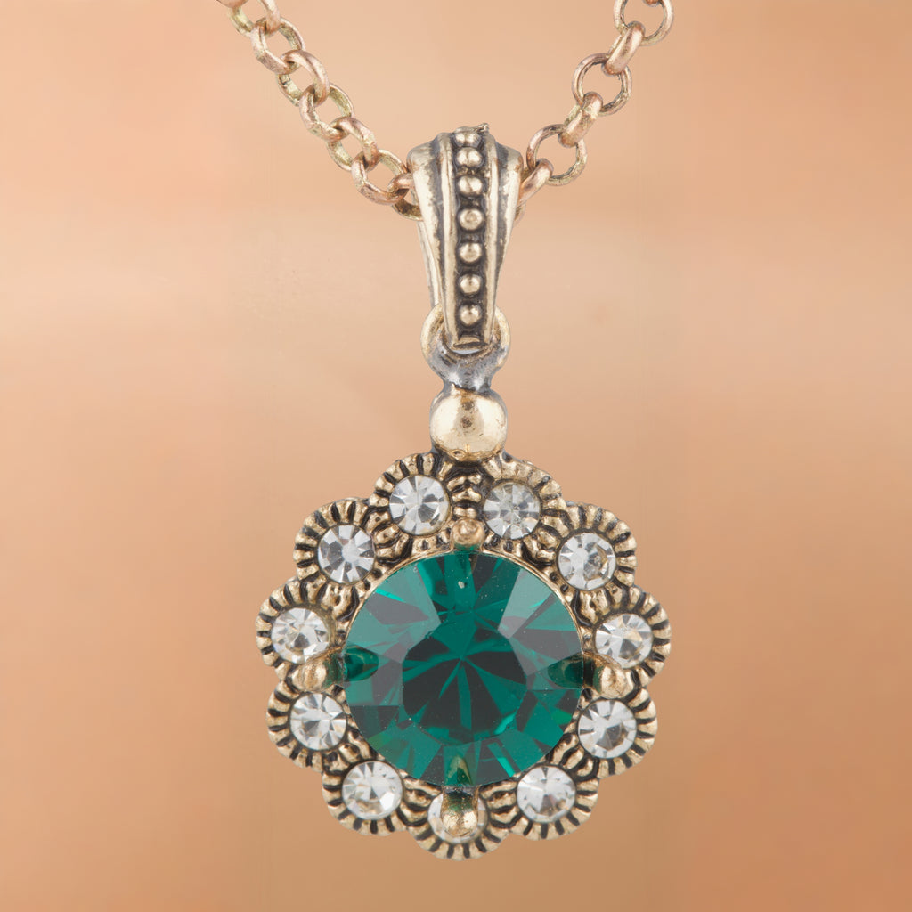 Gold necklace with a green gemstone pendant on a beige background