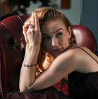 Woman in a dark red dress sitting on a leather chair in a dimly lit room.