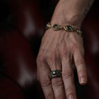 Hand wearing a gold ring and bracelet against a dark background