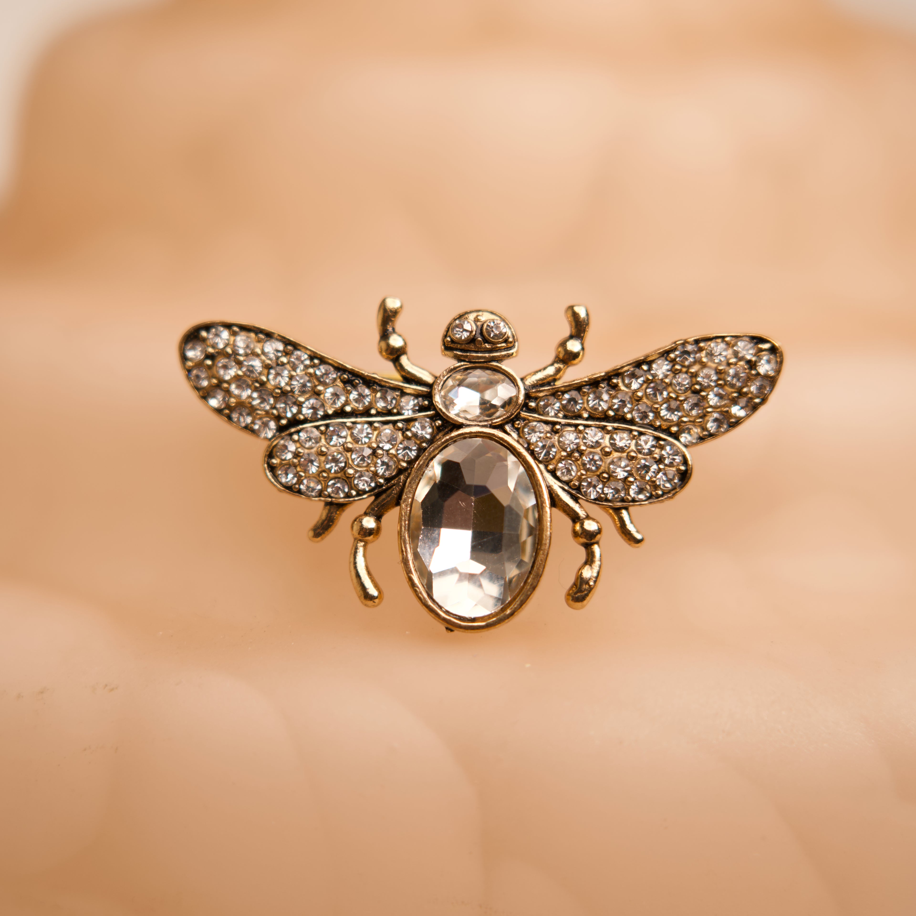 Gold bee-shaped brooch with rhinestones on a beige background