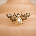 Gold bee-shaped brooch with pearl accents on a mannequin