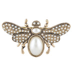 Decorative bee-shaped object with pearl-like stones on a white background