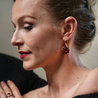Woman wearing colorful earrings and a black top with colorful accents.