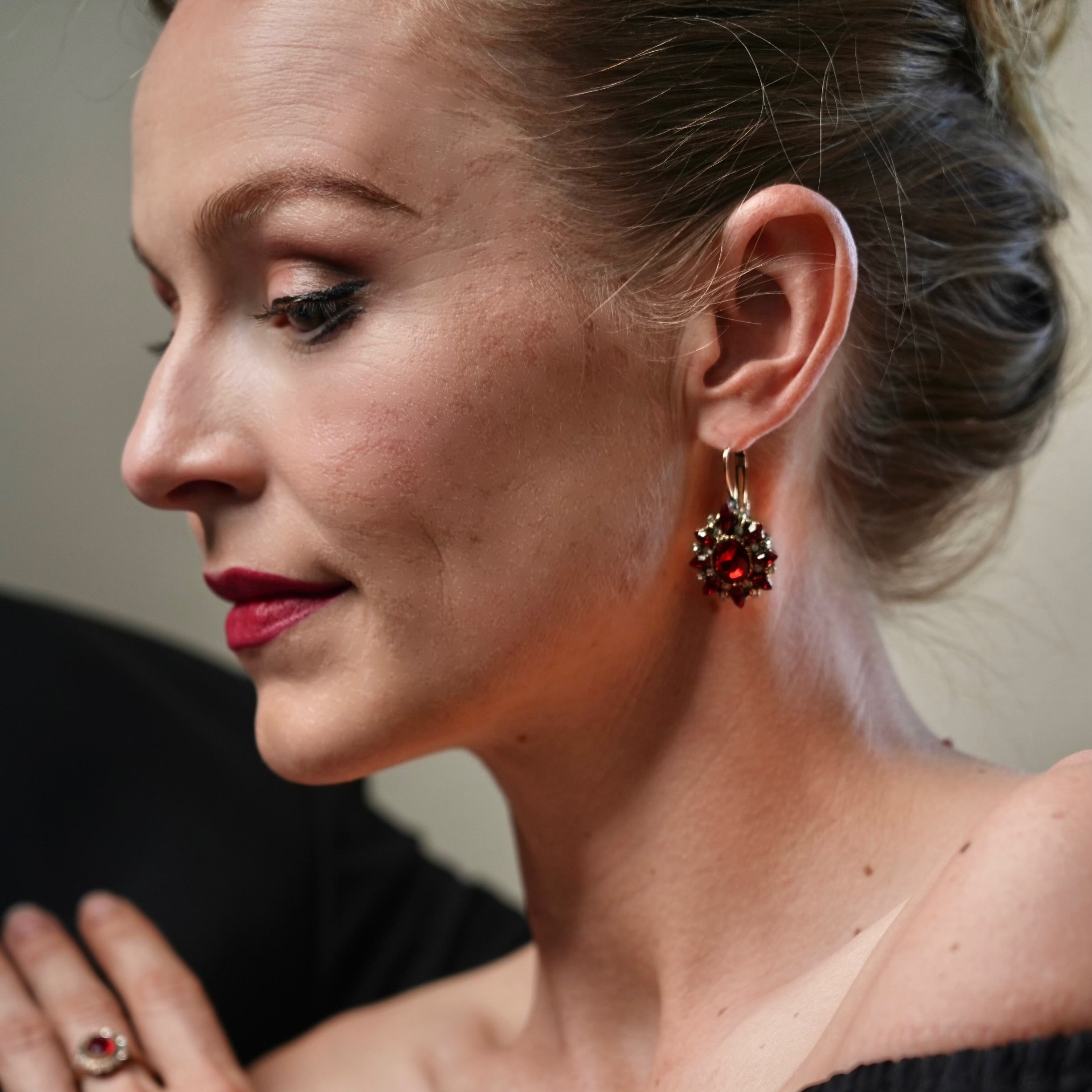 Woman wearing colorful earrings and a black top with colorful accents.