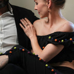 Person wearing a black off-shoulder top with colorful pom-poms sitting on a couch.