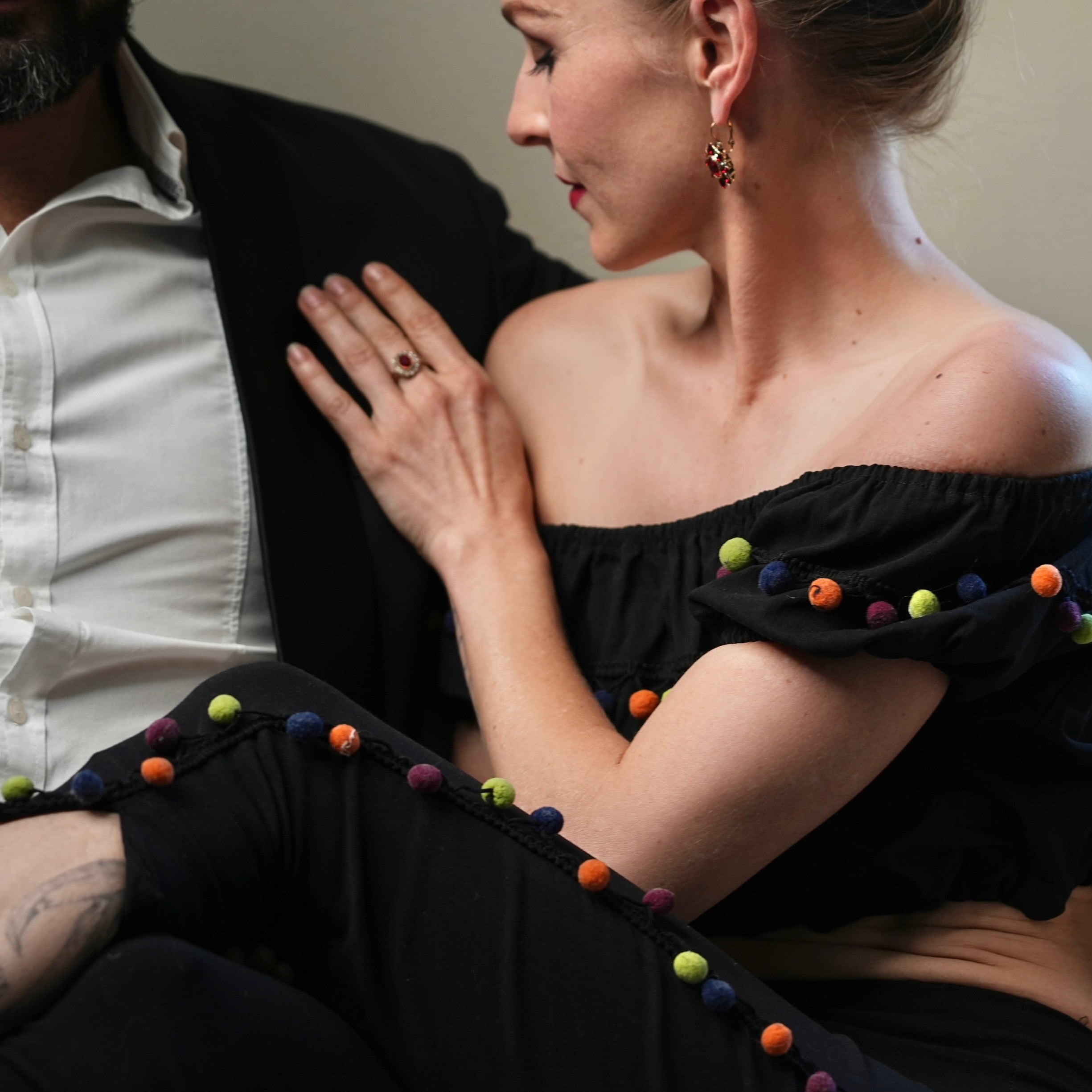 Person wearing a black off-shoulder top with colorful pom-poms sitting on a couch.
