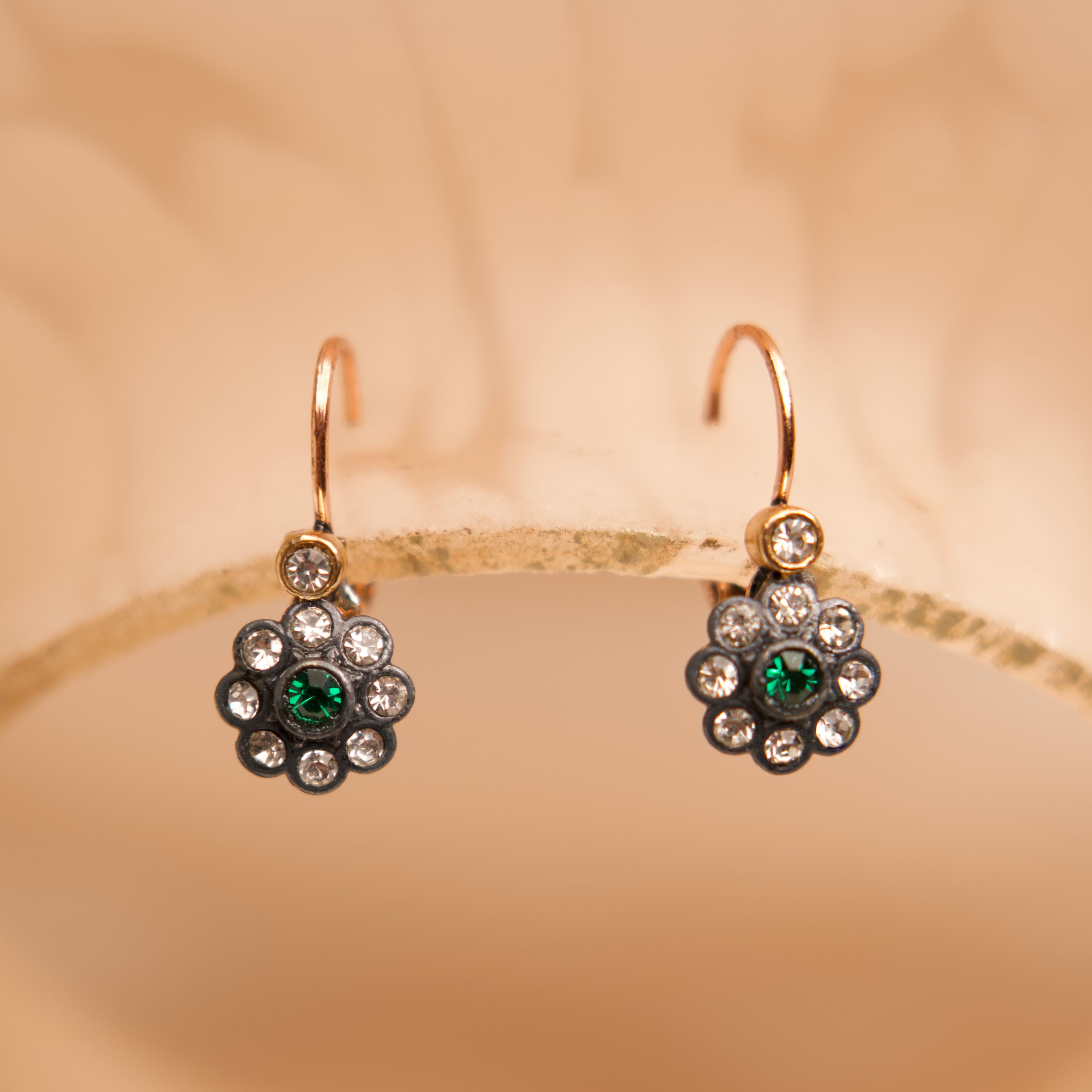 Pair of floral earrings with green gemstones on a beige background