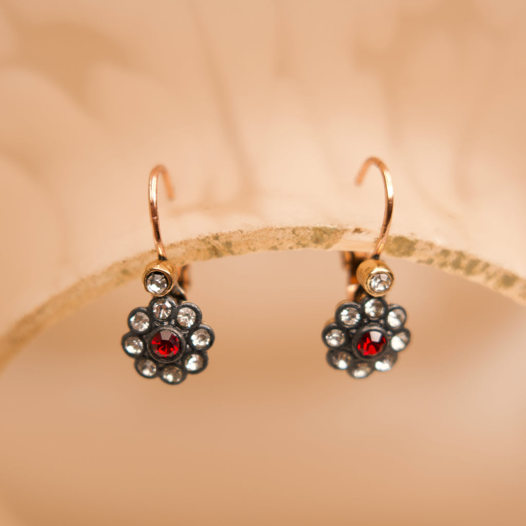 Gold earrings with red gemstones on a beige background