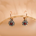Gold earrings with red gemstones on a beige background