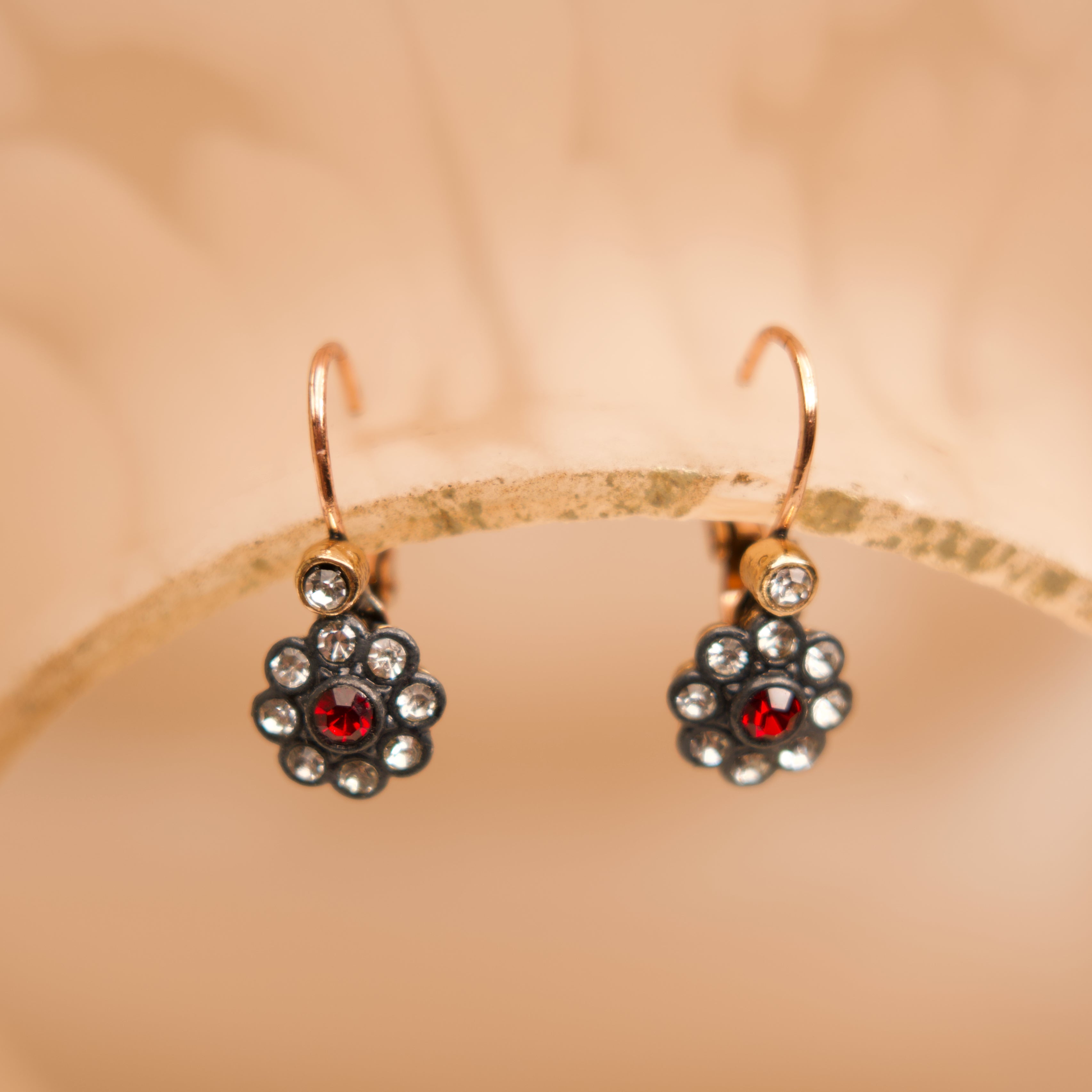 Gold earrings with red gemstones on a beige background