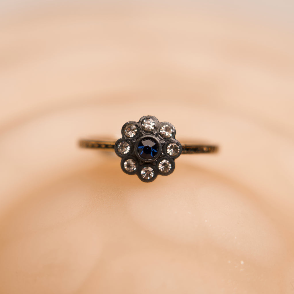 Ring with a central blue gemstone and smaller diamonds on a beige background