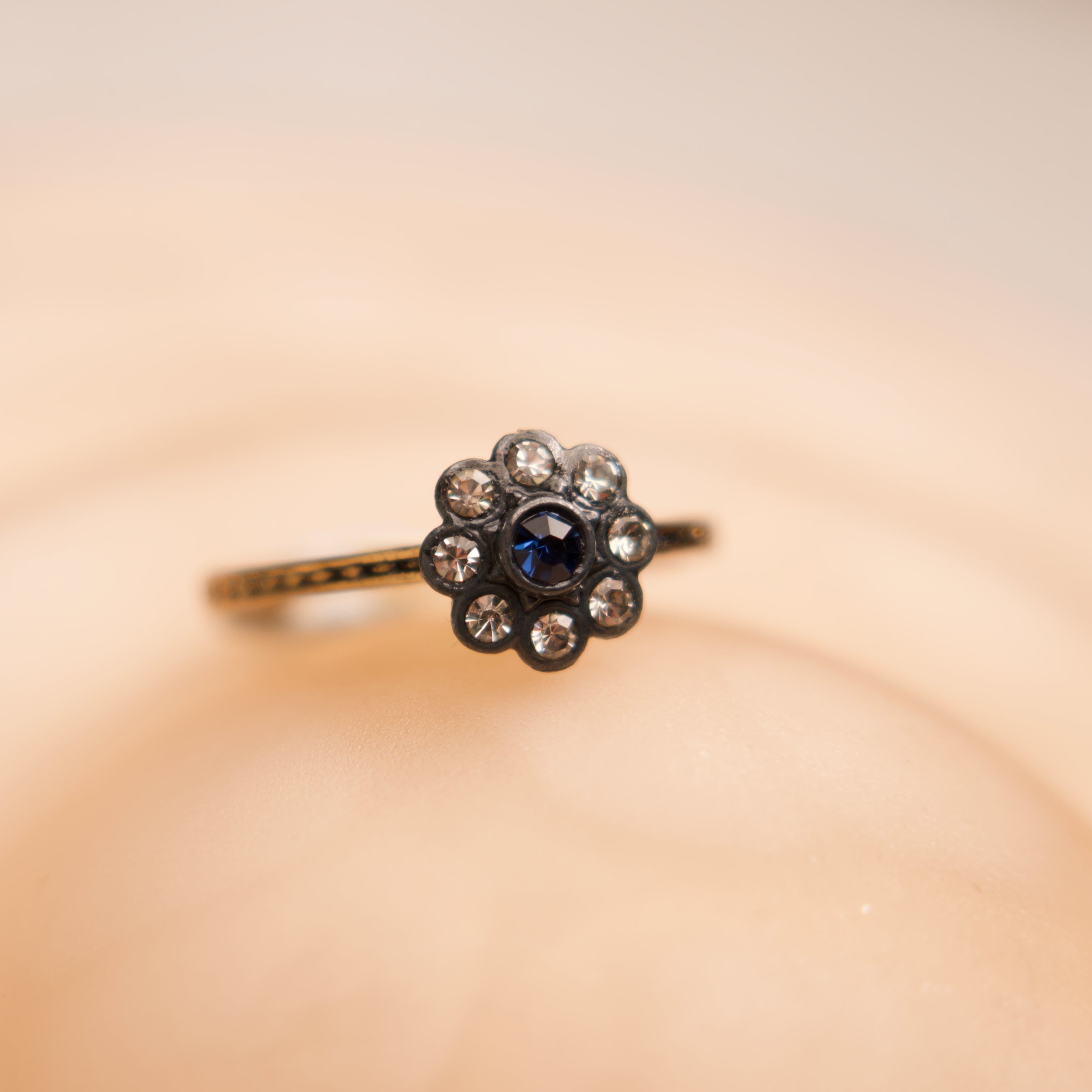 Ring with a central blue gemstone and diamond-studded floral design on a beige background