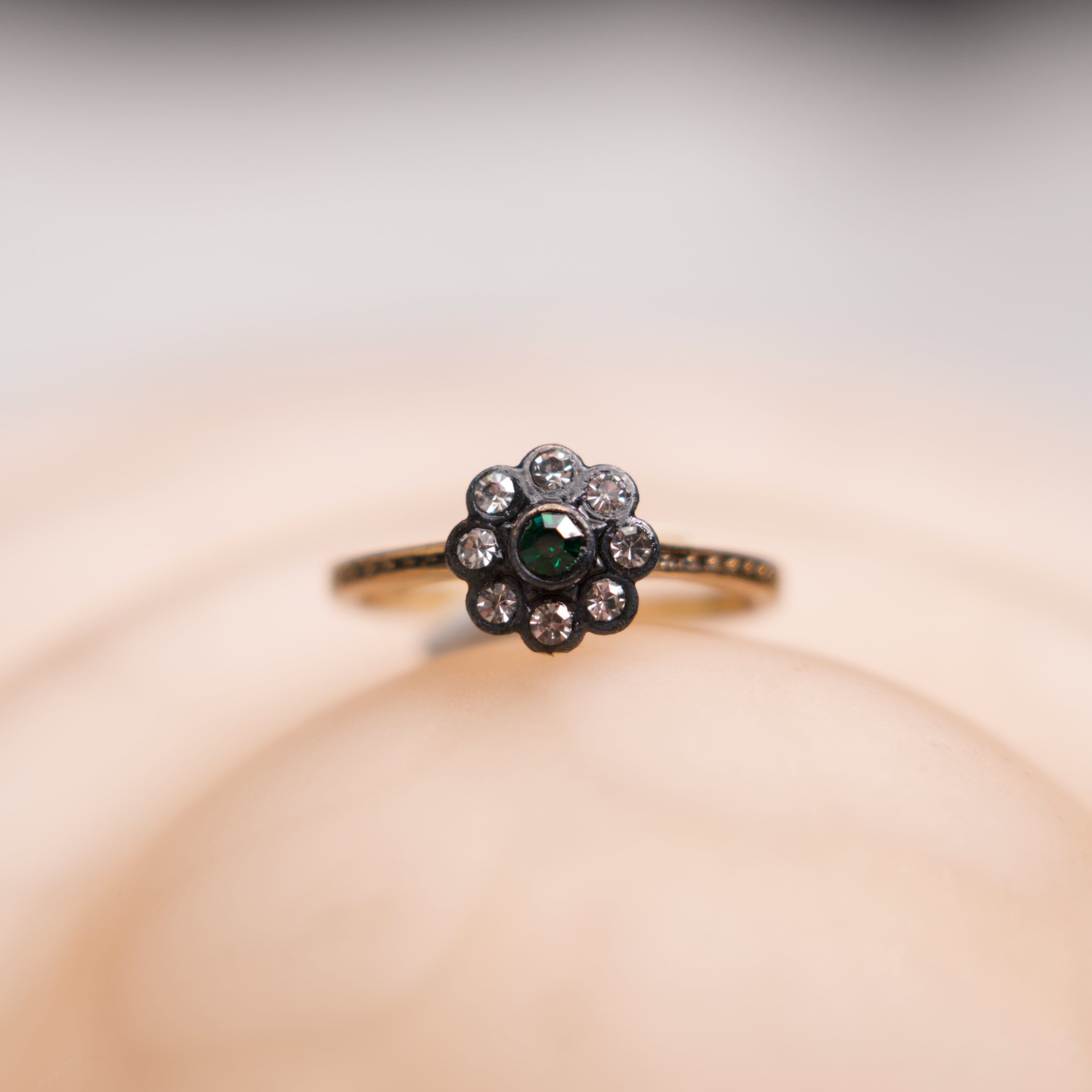 Ring with a green gemstone and diamond accents on a soft beige background