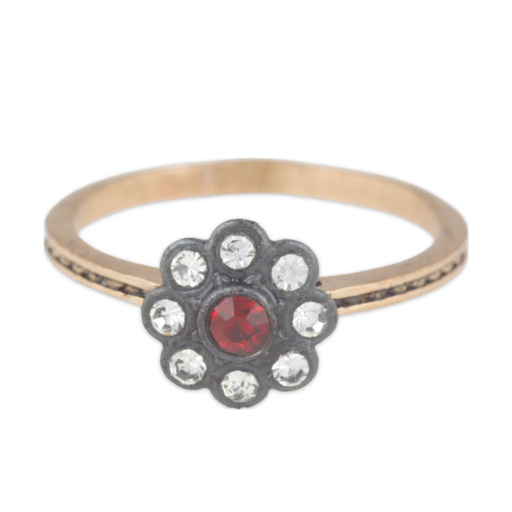 Gold ring with a flower-shaped black setting featuring red gemstone and clear crystals on a white background.