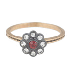 Gold ring with a flower-shaped black setting featuring red gemstone and clear crystals on a white background.