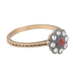 Gold ring with a decorative flower head featuring red gemstone and clear crystals on a white background