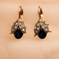 Pair of earrings with blue gemstones and gold accents on a beige background