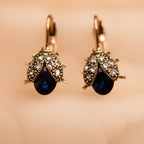 Pair of earrings with blue gemstones and gold accents on a beige background