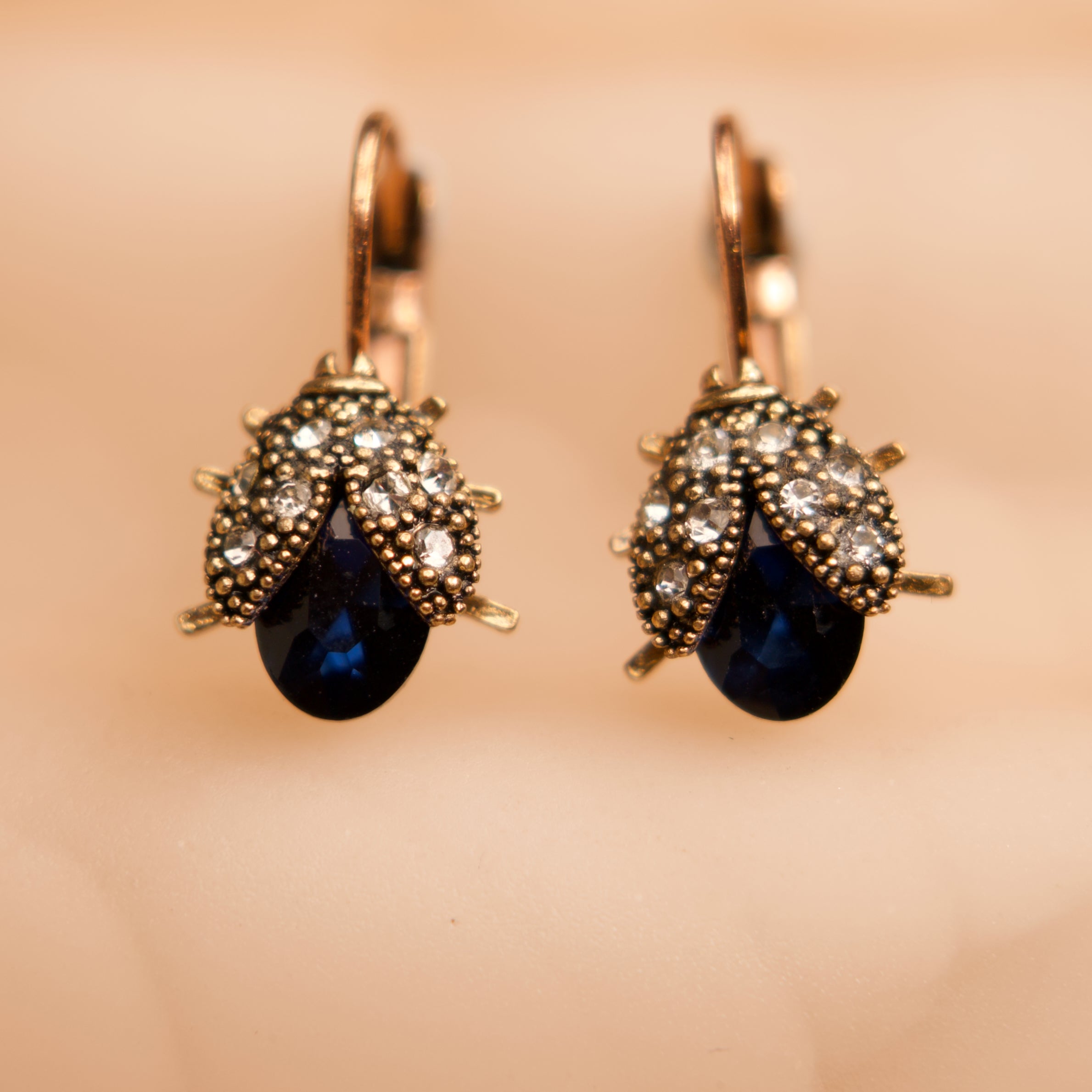 Pair of earrings with blue gemstones and gold accents on a beige background